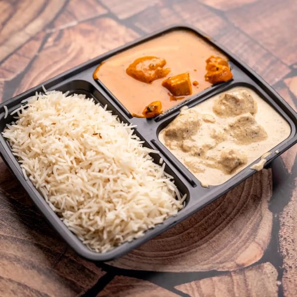 A black takeout container with rice, butter chicken, and chicken malai tikka on a wooden surface.