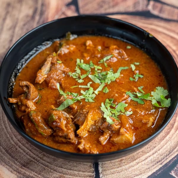 A black bowl filled with a rich, orange-brown curry, garnished with fresh green cilantro.