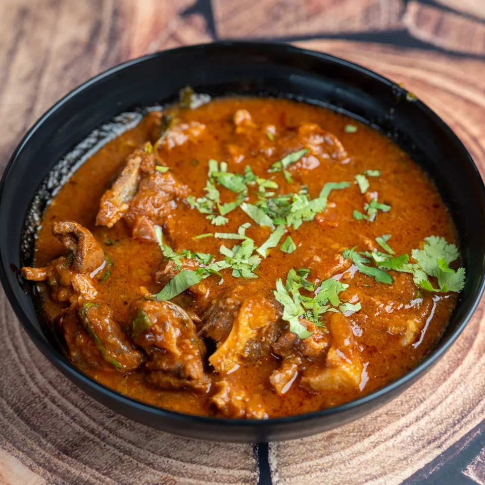 A black bowl filled with a rich, orange-brown curry, garnished with fresh green cilantro.
