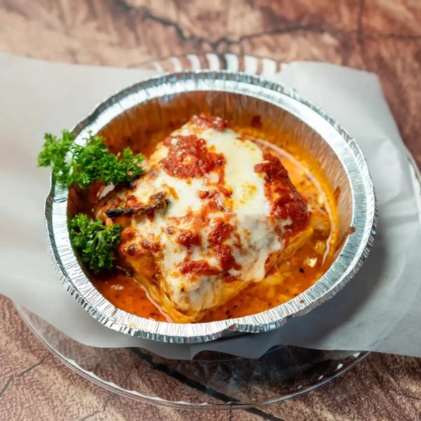 Baked lasagna with melted cheese and red sauce in a foil container, garnished with parsley.