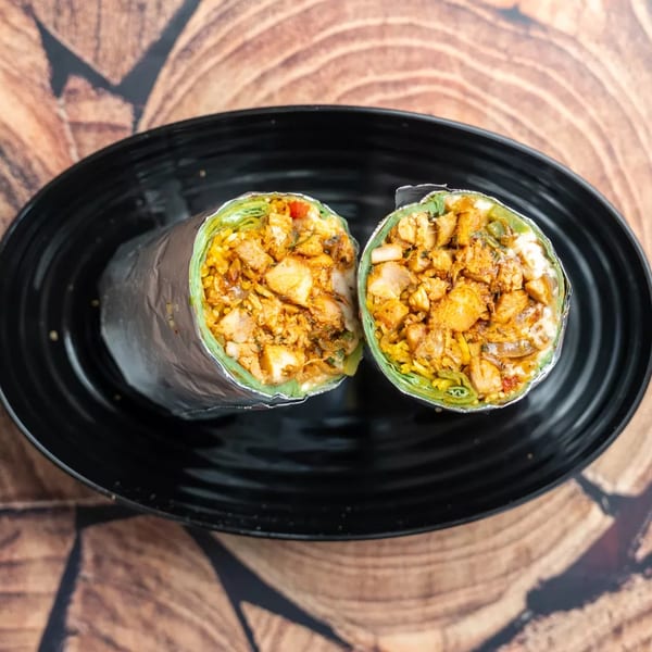 Two halves of a chicken and rice burrito, wrapped in foil, on a black plate.
