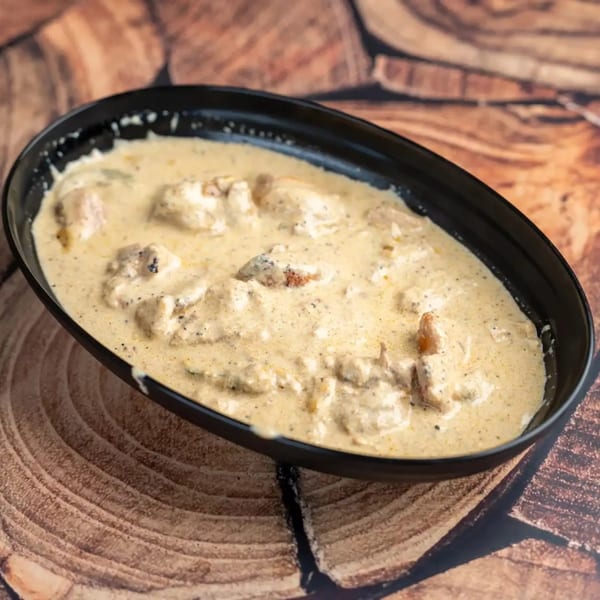 Creamy chicken curry in a black oval bowl, resting on a rustic wooden surface.