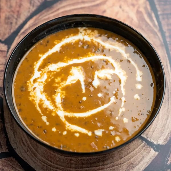 A black bowl of creamy orange Dal Makhani with a white cream swirl on a wooden surface.