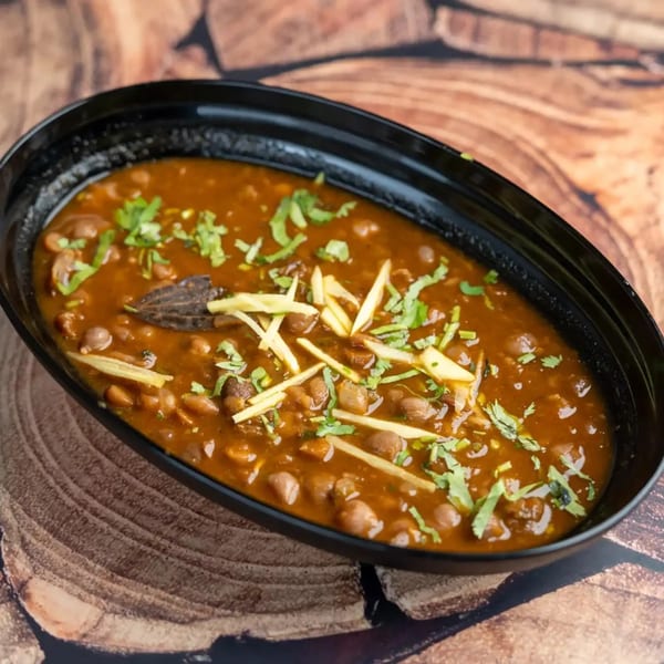 A black bowl of chana masala, garnished with fresh cilantro and ginger, on a wooden surface.