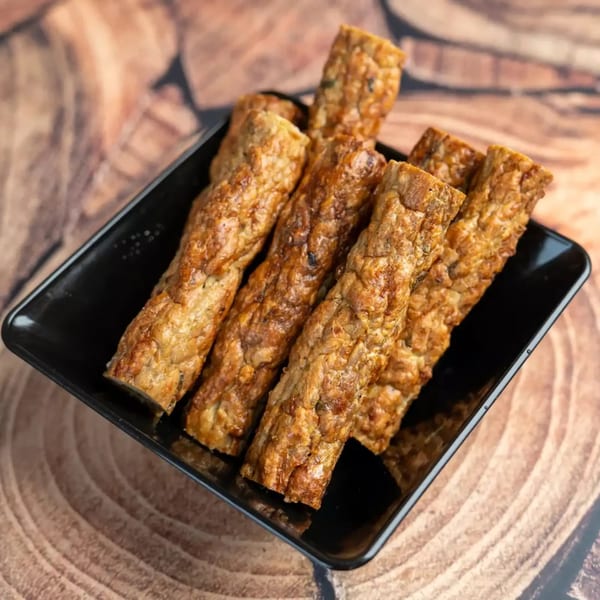 Golden brown fried tempeh sticks arranged in a black rectangular dish on a wooden surface.
