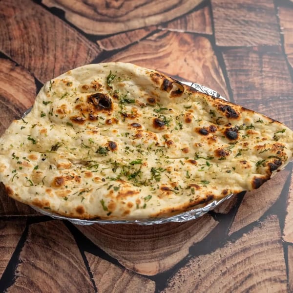 Garlic naan bread, garnished with green herbs, served in foil on a wooden surface.