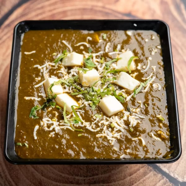 Palak Paneer, a vibrant green spinach curry with cubes of paneer cheese, garnished with cilantro.