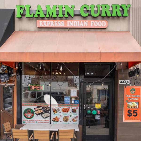 Exterior of Flamin Curry, an Indian restaurant, with an orange awning, outdoor seating, and menu posters.