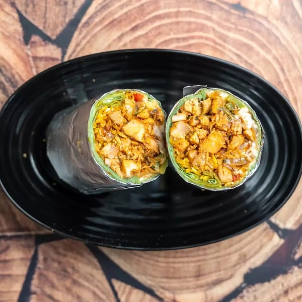 Two halves of a chicken and rice burrito, wrapped in foil, on a black plate.