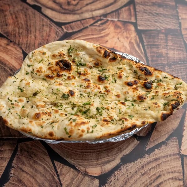 Garlic naan bread, topped with green herbs, served in foil on a wooden surface.