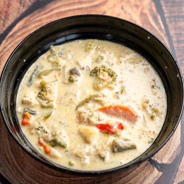Creamy vegetable soup with broccoli, red peppers, and other vegetables in a black bowl.